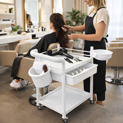 Woman getting hair treatment in a salon with a stylist and tools on a cart.